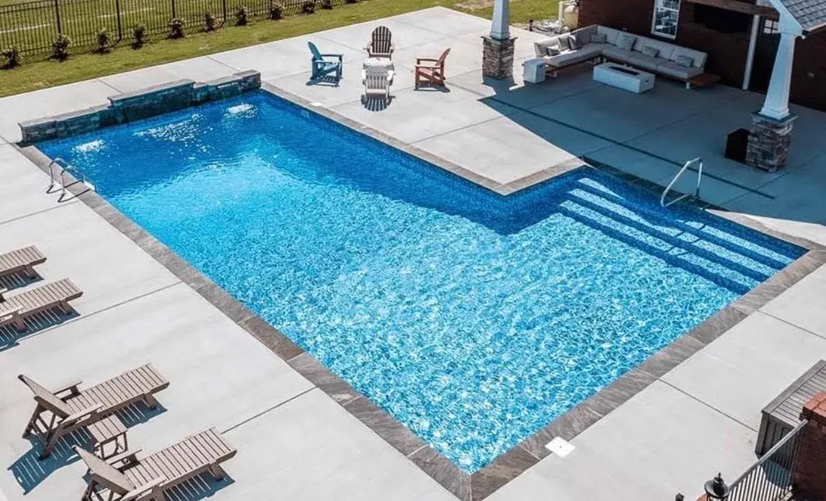 Renovated inground pool with tanning ledge and outdoor stone fireplace at dusk